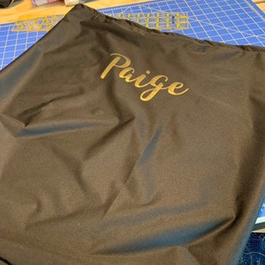 May include: A black fabric storage bag with the name "Paige" embroidered in gold lettering.