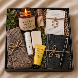 Peut inclure: Un coffret cadeau avec une bougie, des allumettes, des chaussettes, un baume à lèvres, du savon, une crème pour les mains, un carnet et un stylo. La bougie dit "smells like you're appreciated". La carte dit "YOU ARE AN ESSENTIAL PIECE OF OUR TEAM!"