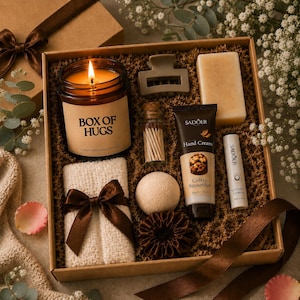May include: A gift box filled with self-care items. Includes a lit candle labeled "BOX OF HUGS", a bar of soap, hand cream, lip balm, a hair clip, a small towel with a bow, a bath bomb, matches, and a hair scrunchie. The box is decorated with a brown ribbon.