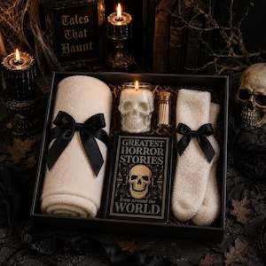 May include: A gift box containing a cream-coloured rolled blanket with a black ribbon, a cream-coloured pair of fuzzy socks with a black ribbon, a skull-shaped candle, a small glass vial of matches, and a book titled Greatest Horror Stories from Around the World.