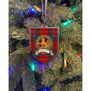 May include: A shield-shaped Christmas tree ornament with a red plaid pattern. The ornament features a gold emblem with a tiger and the text "TOUCH NOT THE CAT BOT A GLOVE". Below the emblem is a banner that reads "MacPherson". The ornament hangs from a silver ribbon.