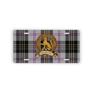 Peut inclure: Une plaque d'immatriculation en tartan gris et noir avec une bordure violette. Au centre de la plaque se trouve un blason avec un chat doré, le texte "Touch Not The Cat Bot A Glove" et le nom "MacPherson".