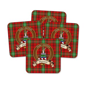 May include: A set of four square coasters featuring a red, green, and white tartan plaid pattern. Each coaster displays a circular crest with a hand holding a sword above a castle, the text "DUN EISTEIN" and the name "Morrison" on a banner.