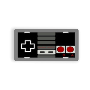 Peut inclure: Une manette de jeu vidéo noire et grise avec un signe plus blanc, des boutons gris marqués "Select" et "Start", et deux boutons rouges marqués "B" et "A".