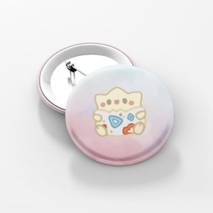 May include: Two round, light pink pinback buttons. One button is lying flat, and the other is upright. The buttons feature a cartoon Togepi character on a pastel pink and blue background.