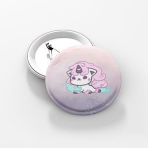 May include: Two round, white-backed buttons. One button features a cartoon unicorn-cat with pink hair, a purple horn, and a light blue cloud. The background is a gradient of pink and purple with white speckles. The second button is blank.