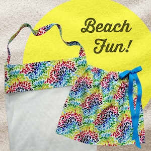 May include: A white mesh beach bag with a colorful floral print top and a matching colorful floral print skirt with a blue ribbon. The text "Beach Fun!" is on a yellow circle.