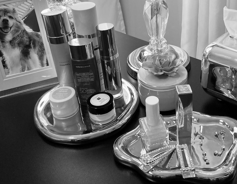May include: A silver tray with a variety of beauty products, including a bottle of Chanel lotion, a bottle of sunscreen, a jar of face cream, and a bottle of nail polish. The tray is on a black surface.
