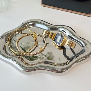 May include: A silver, wavy, decorative tray with two gold bracelets and a gold watch with a digital display.