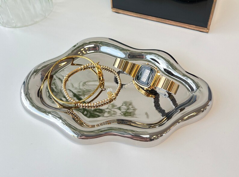 May include: A silver, wavy, decorative tray with two gold bracelets and a gold watch with a digital display.