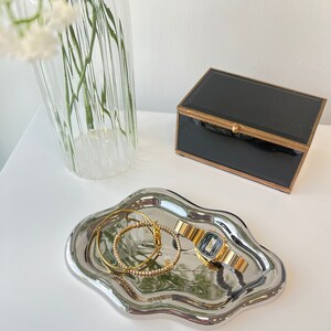 May include: A silver, wavy, decorative tray with a gold watch and two gold bracelets on it.