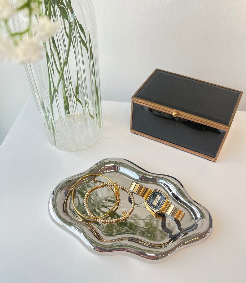 May include: A silver, wavy, decorative tray with a gold watch and two gold bracelets on it.