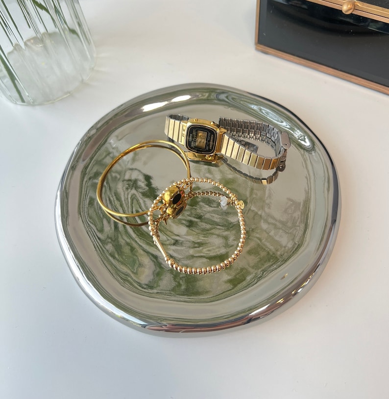May include: A silver tray with a marbled design in shades of green and white. The tray features a gold watch, a gold bracelet, and a gold ring.