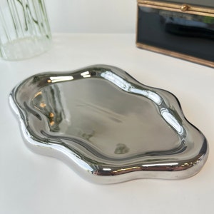 May include: A silver, wavy, decorative tray with a smooth, reflective surface.