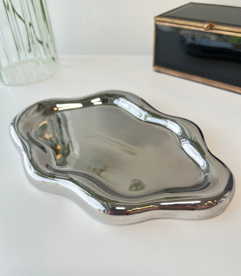May include: A silver, wavy, decorative tray with a smooth, reflective surface.