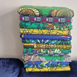 May include: A stack of 12 colorful fabric pieces with various patterns, including geometric designs, floral motifs, and abstract shapes. The fabrics are primarily green, yellow, blue, and red.
