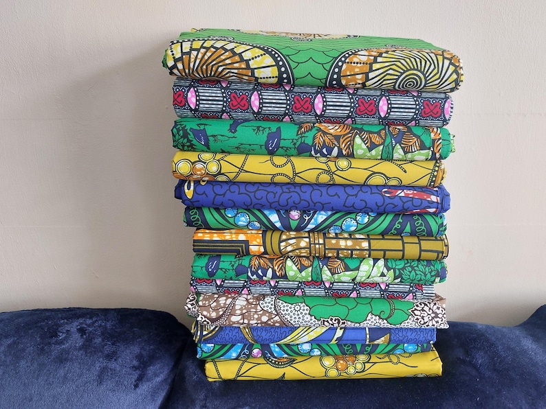 May include: A stack of 12 colorful fabric pieces with various patterns, including geometric designs, floral motifs, and abstract shapes. The fabrics are primarily green, yellow, blue, and red.