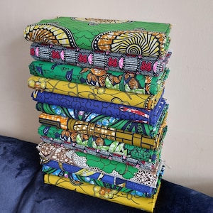 May include: A stack of 14 colorful fabric pieces with various patterns, including green, yellow, blue, red, and brown. The fabric is folded and stacked neatly.