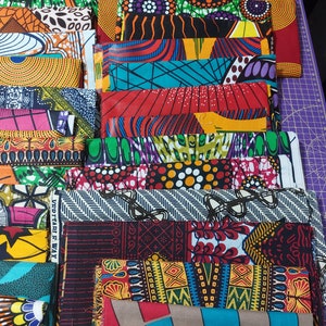 May include: A stack of colorful fabric squares with various patterns, including geometric designs, floral motifs, and abstract shapes. The fabrics are arranged in a layered fashion, showcasing a vibrant and eclectic mix of colors and textures.