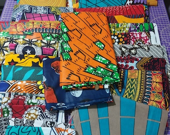 May include: A collection of colorful fabric squares with various geometric and abstract patterns. The fabrics are arranged in a pile on a purple surface.