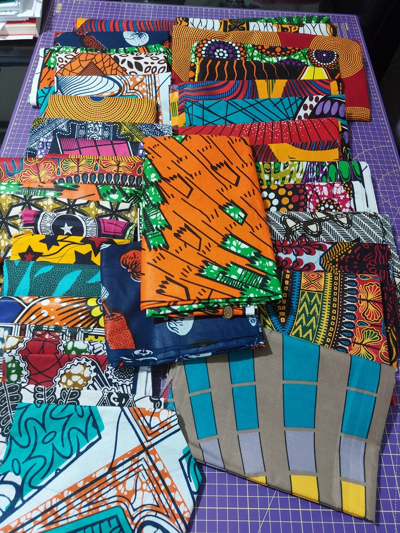 May include: A collection of colorful fabric squares with various geometric and abstract patterns. The fabrics are arranged in a pile on a purple surface.