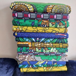 May include: A stack of 12 colorful fabric prints with various patterns, including geometric, floral, and abstract designs. The fabrics are mostly green, yellow, blue, and orange.
