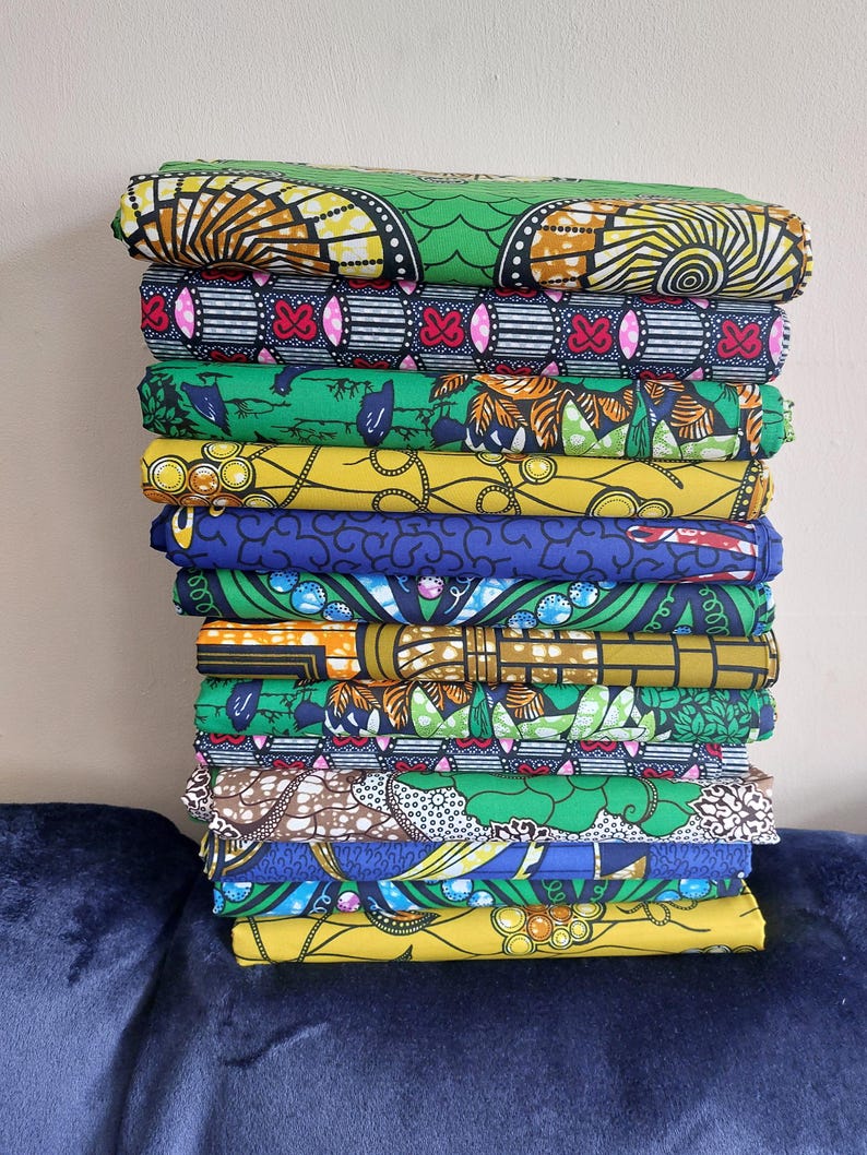 May include: A stack of 12 colorful fabric prints with various patterns, including geometric, floral, and abstract designs. The fabrics are mostly green, yellow, blue, and orange.