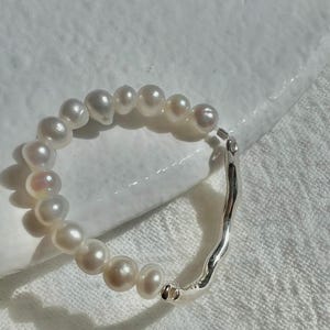May include: A silver ring with a wavy band and a row of white pearls.