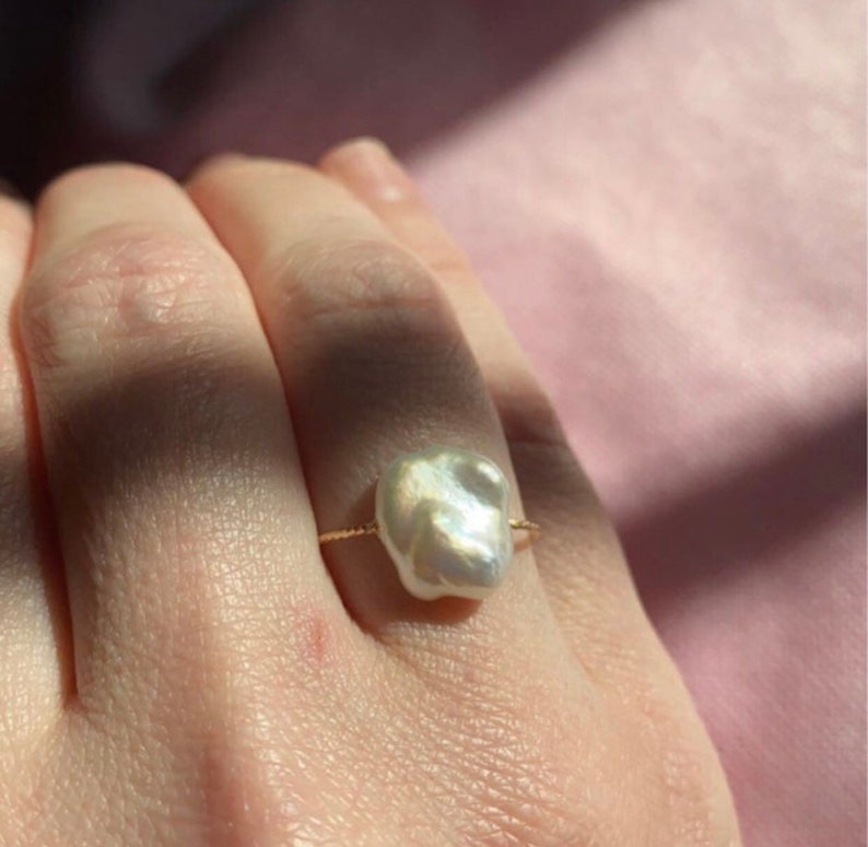 May include: A gold ring with a large, irregular, white pearl. The pearl is set in a simple band.