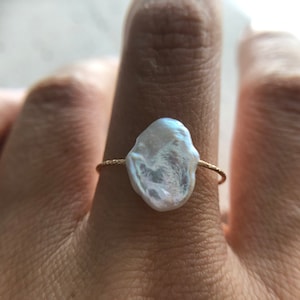 May include: A gold ring with a large, irregular, white pearl. The pearl is set on a thin gold band.