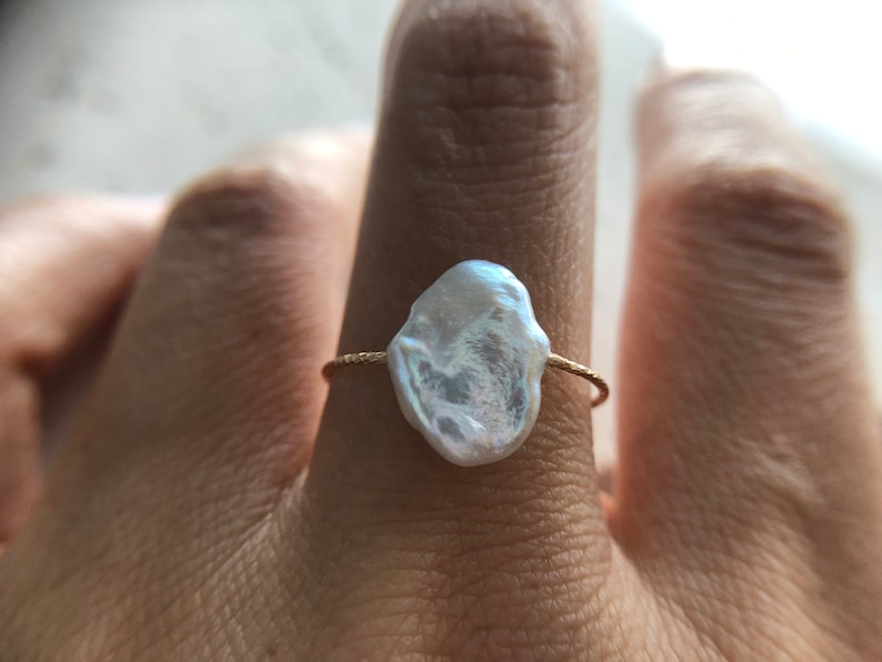 May include: A gold ring with a large, irregular, white pearl. The pearl is set on a thin gold band.