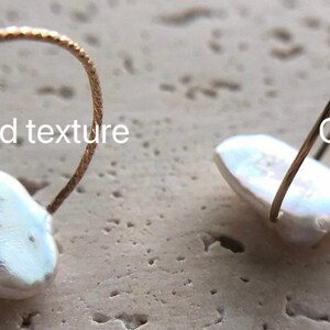 May include: Two gold filled rings with a white pearl. One ring has a textured band and the other has a smooth band. The text "Gold filled texture" is above the ring with the textured band. The text "Gold filled glaze" is above the ring with the smooth band.