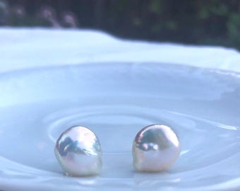 May include: Two iridescent white pearl earrings on a white saucer.