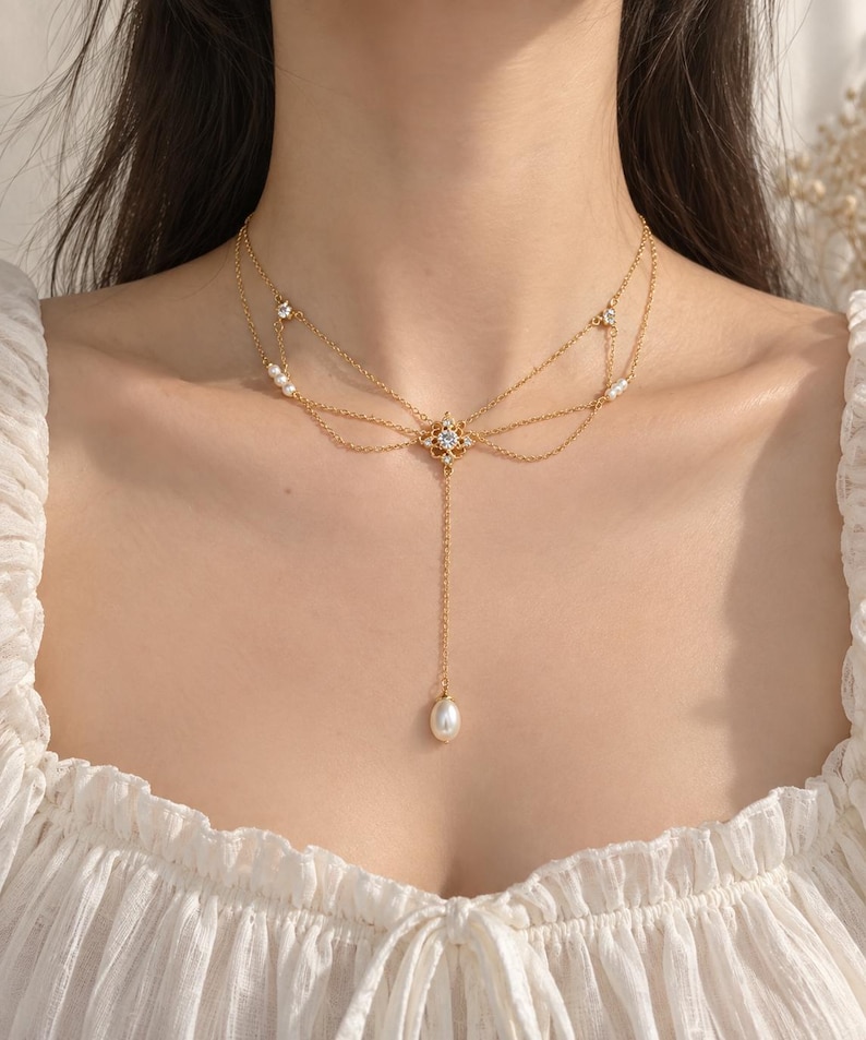 Puede incluir: Un collar dorado de varias hebras con cadenas delicadas dispuestas en un dise&ntilde;o superpuesto. El centro presenta un peque&ntilde;o colgante en forma de estrella con una piedra clara, acentuado por peque&ntilde;as perlas blancas y piedras claras adicionales.