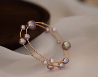 Peut inclure: Un bracelet délicat en or avec une double rangée de perles. Les perles sont d'un violet doux et iridescent et de tailles différentes.