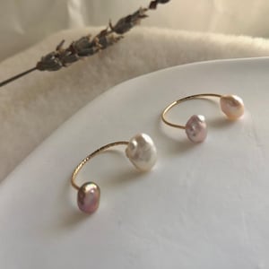 May include: Two gold rings with pearl accents. One ring has a white pearl and a pink pearl, the other ring has two pink pearls.
