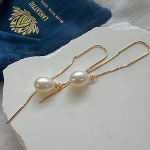 May include: A pair of gold chain earrings with a pearl drop on each side. The earrings are long and dangle from the earlobe.