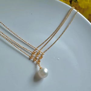 Puede incluir: Un collar de oro con tres cadenas delicadas y un colgante de perla.
