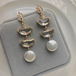 Pode incluir: Um par de brincos de ouro com três formas de lágrima de cristal transparente e uma gota de pérola em cada brinco.