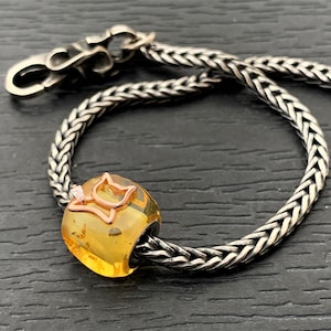 Op de afbeelding: Een zilveren kettingarmband met een gele amber kralen met een roségouden kat charme.