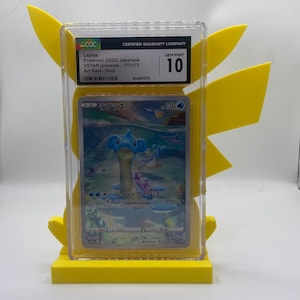 May include: A graded Lapras Pokémon card from the VSTAR Universe set, featuring a holographic art rare design. The card is encased in a clear protective holder and is graded a GEM MINT 10 by CGC. The card is displayed on a yellow Pikachu-themed stand.