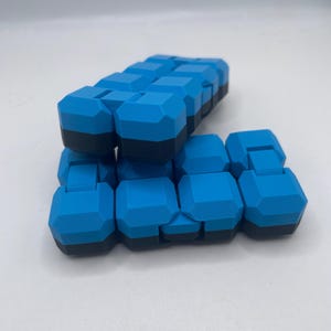 May include: A blue and black fidget toy, composed of multiple connected geometric shapes. The toy is in two stacks, with the top one partially obscuring the bottom. The shapes are a vibrant blue with black bases.