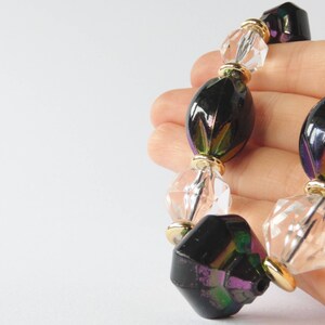 May include: A necklace with iridescent black and clear glass beads. The beads are oval and faceted, and the necklace is strung on a gold chain.