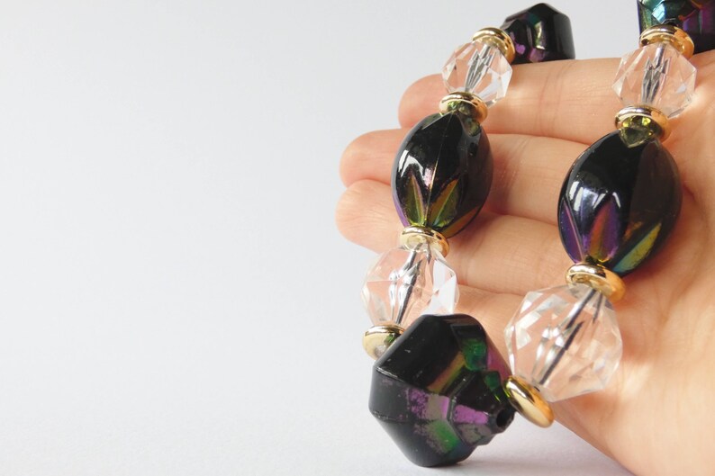 May include: A necklace with iridescent black and clear glass beads. The beads are oval and faceted, and the necklace is strung on a gold chain.