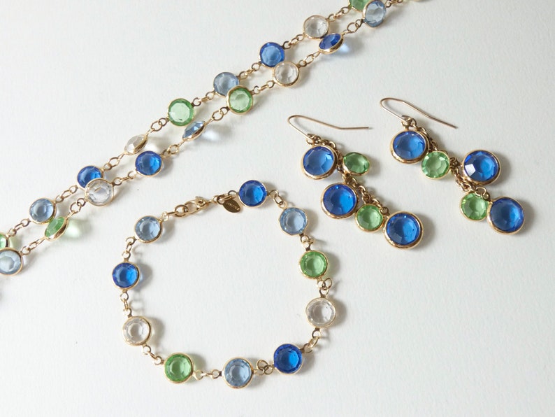 K&ouml;nnte beinhalten: Ein Schmuckset mit einer Halskette, einem Armband und Ohrringen. Die St&uuml;cke bestehen aus einer goldenen Kette und haben blaue, gr&uuml;ne und klare Glasperlen.