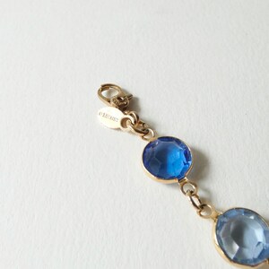 K&ouml;nnte beinhalten: Ein goldenes Kettenarmband mit blauen und hellblauen Kristall-Akzenten. Der Verschluss tr&auml;gt die Gravur "ORCHID".