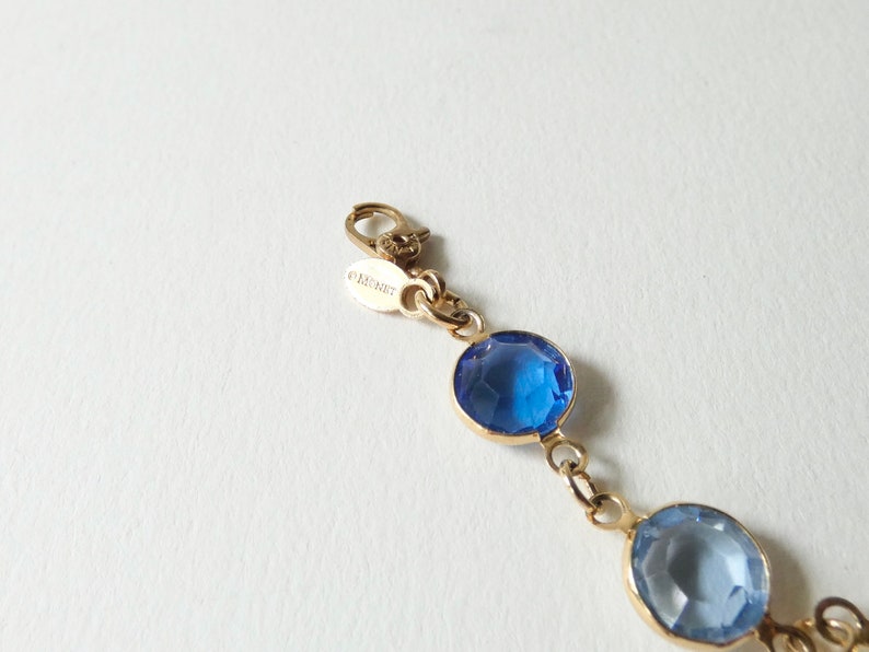 K&ouml;nnte beinhalten: Ein goldenes Kettenarmband mit blauen und hellblauen Kristall-Akzenten. Der Verschluss tr&auml;gt die Gravur "ORCHID".