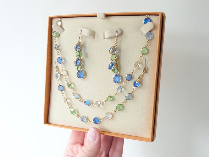 K&ouml;nnte beinhalten: Ein goldfarbenes Halsketten- und Ohrring-Set mit blauen, gr&uuml;nen und klaren Glasperlen. Die Halskette ist mehrlagig und die Ohrringe sind im H&auml;nge-Stil.