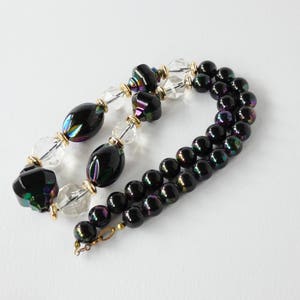 May include: A black and iridescent glass bead necklace with clear glass beads and gold accents.