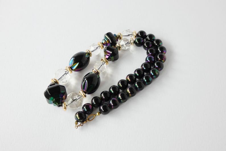 May include: A black and iridescent glass bead necklace with clear glass beads and gold accents.